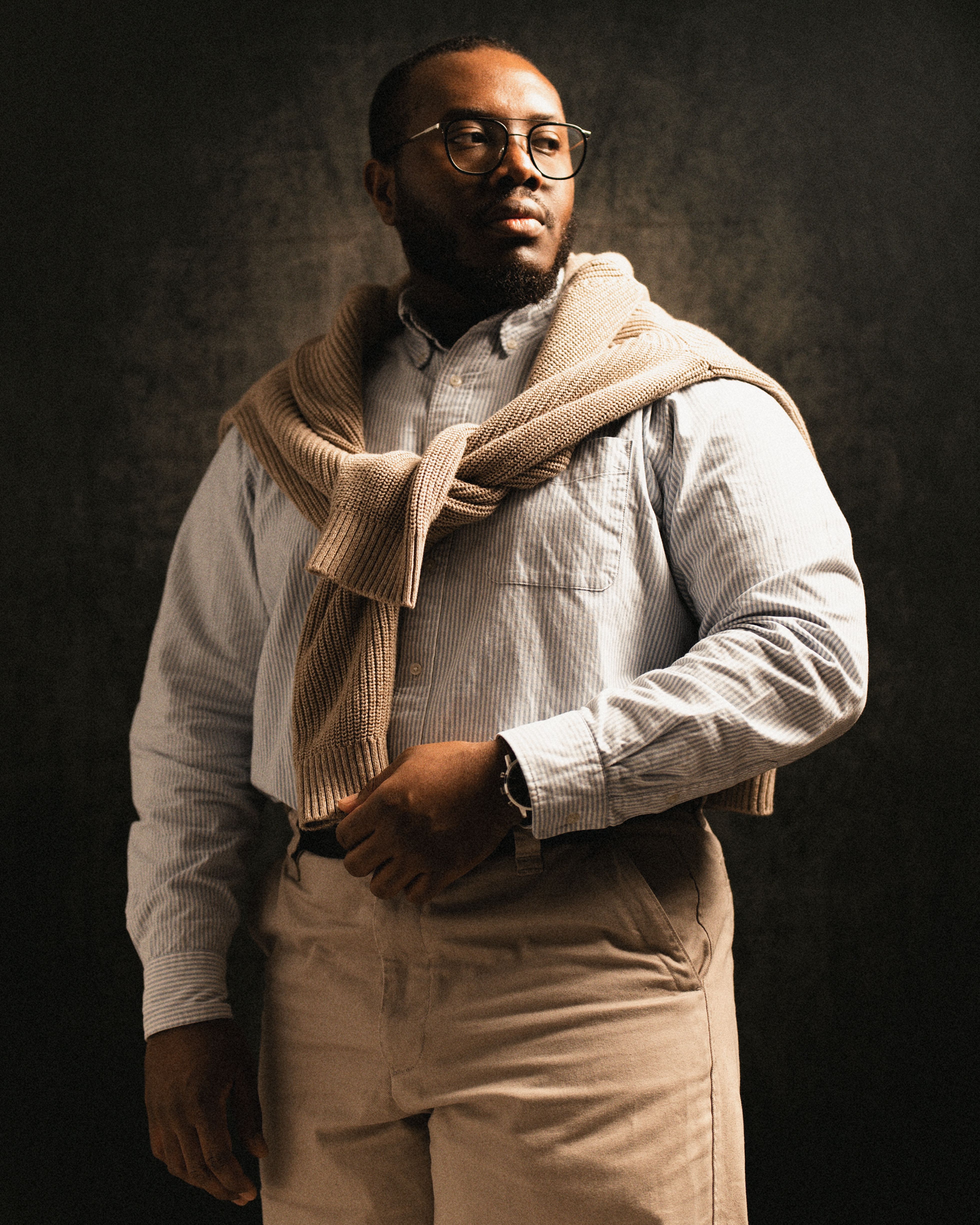 A confident man in glasses and smart casual attire, looking thoughtfully into the distance.