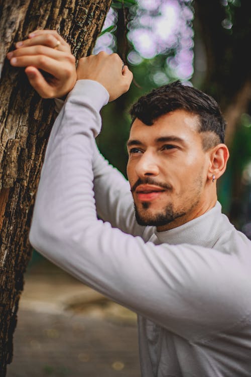 Man in White Long Sleeve Shirt Leaning on Brown Tree Trunk