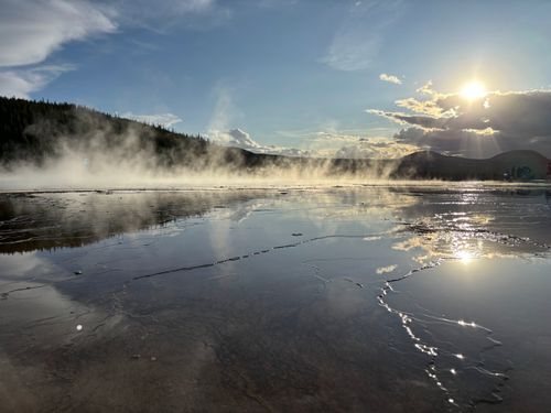 Free Steam rises from a reflective hot spring in Yellowstone under a bright sun. Stock Photo