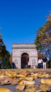 The Arc de Triomphe in Paris surrounded by vibrant autumn foliage and fallen leaves.