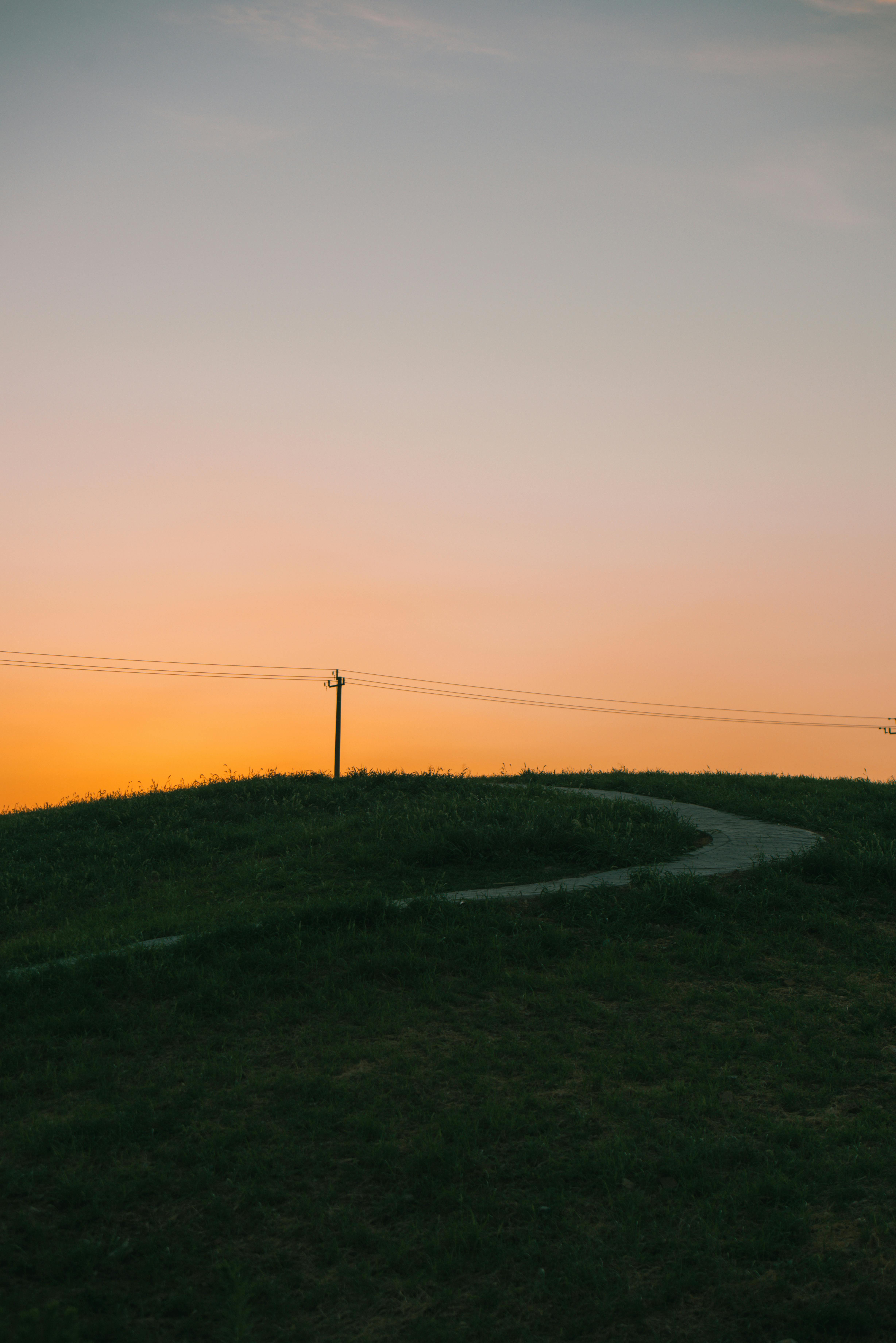 Gratuit Peisaj liniștit la apus, cu o potecă șerpuitoare pe dealuri line sub un cer cald. Fotografie de stoc