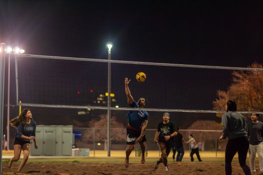 Amateur volleyball players enjoy a dynamic game under the lights in an Arizona park.