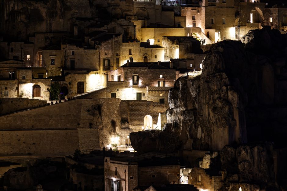 Explore the illuminated ancient architecture of Matera, Italy, captured during nightfall, showcasing unique stone structures.