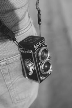 Close-up of a vintage twin-lens camera hanging from a person's waist, in black and white.