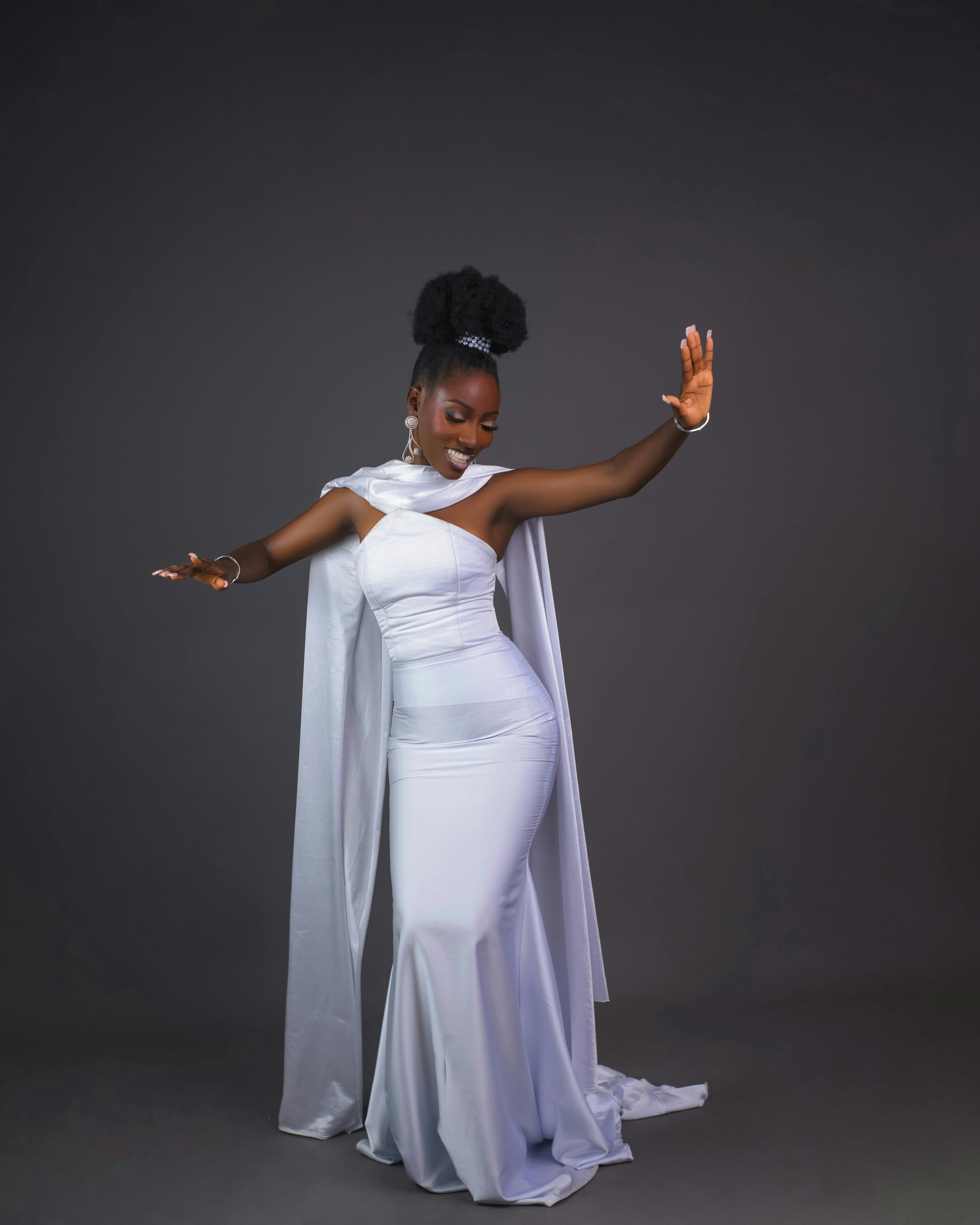 grátis Mulher negra elegante em um vestido branco formal, executando uma graciosa pose de dança em estúdio. Foto profissional
