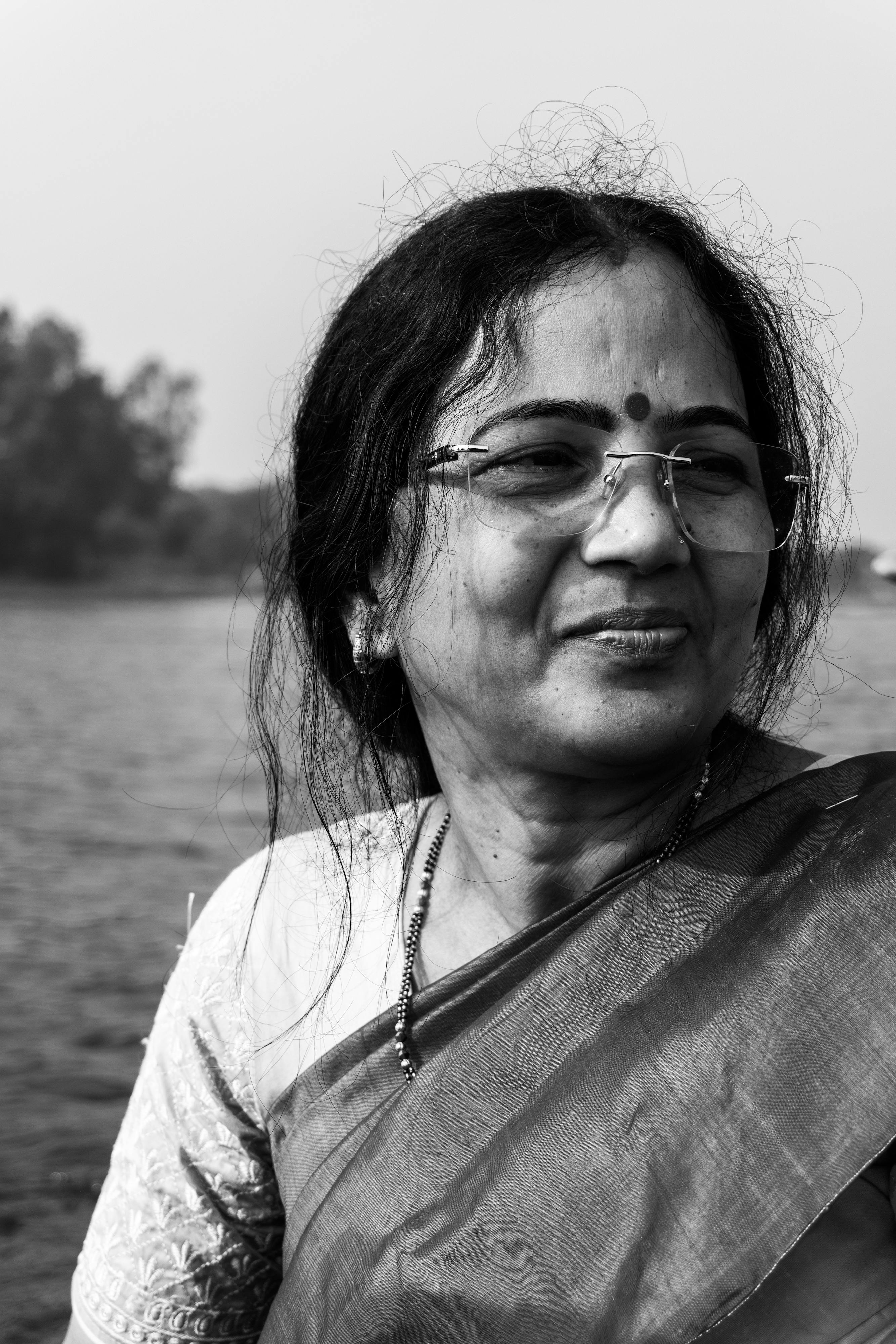 Gratis En eldre kvinne som smiler ved en elvebredde i en tradisjonell sari, fanget i svart-hvitt. Arkivbilde