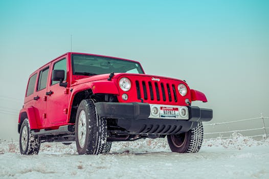Red Jeep SUV parked on a snowy field, showcasing winter driving capability.