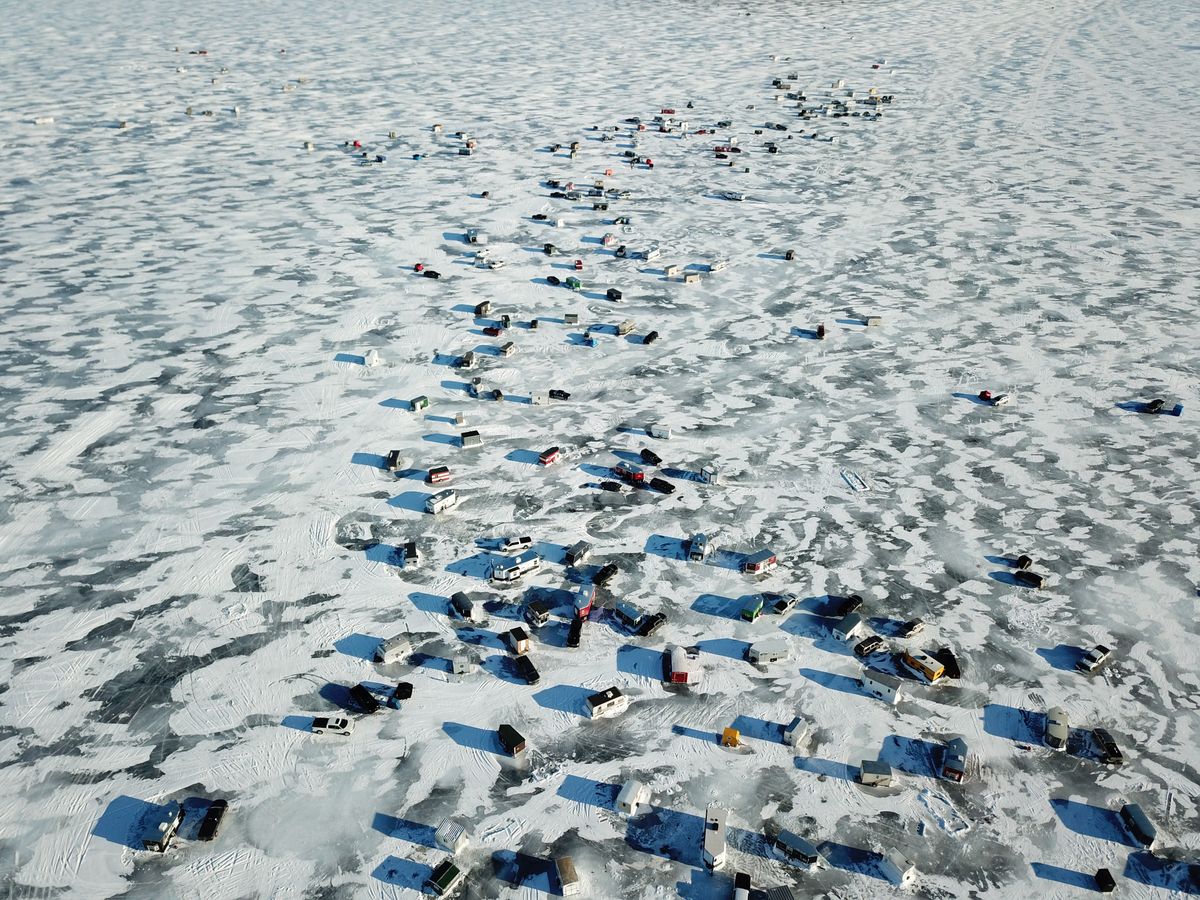 Aerial view of dozens of ice fishing shelters scattered across a frozen lake