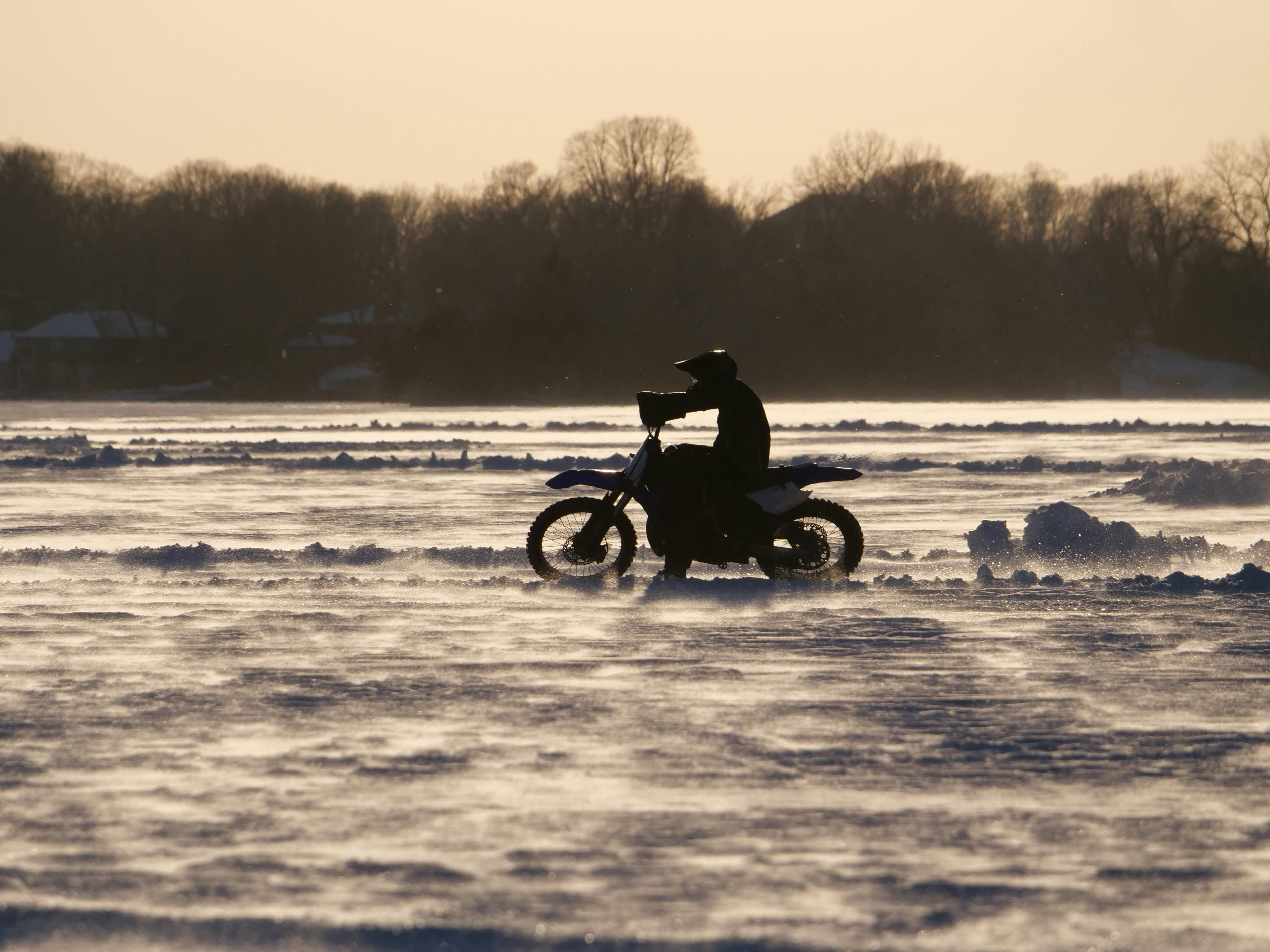 Silhouette of a motorcyclist riding on a snow-covered field at sunset, creating a dramatic scene.