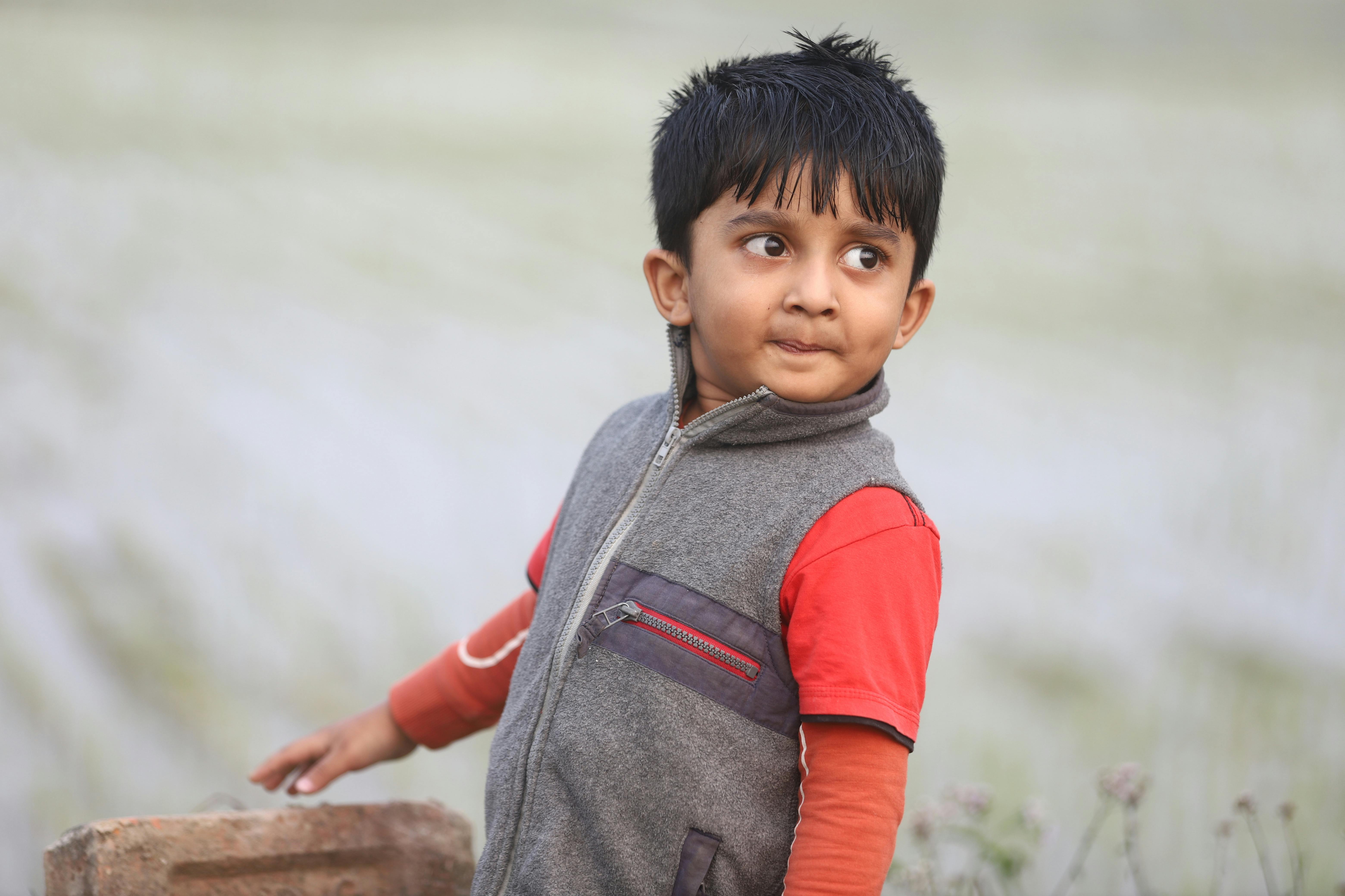 De franc Un noi jove amb una armilla grisa mira amb curiositat en un entorn de camp a l'aire lliure. Foto d'estoc