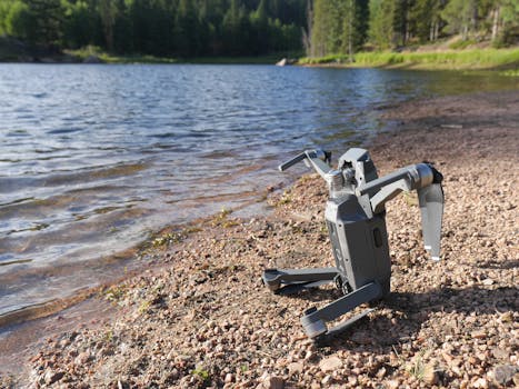A drone rests on a pebble beach by a tranquil lake surrounded by green forest.