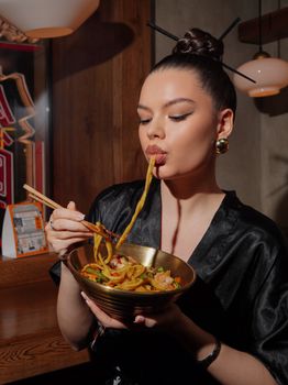 Stylish woman in black kimono enjoying a bowl of noodles at a restaurant.