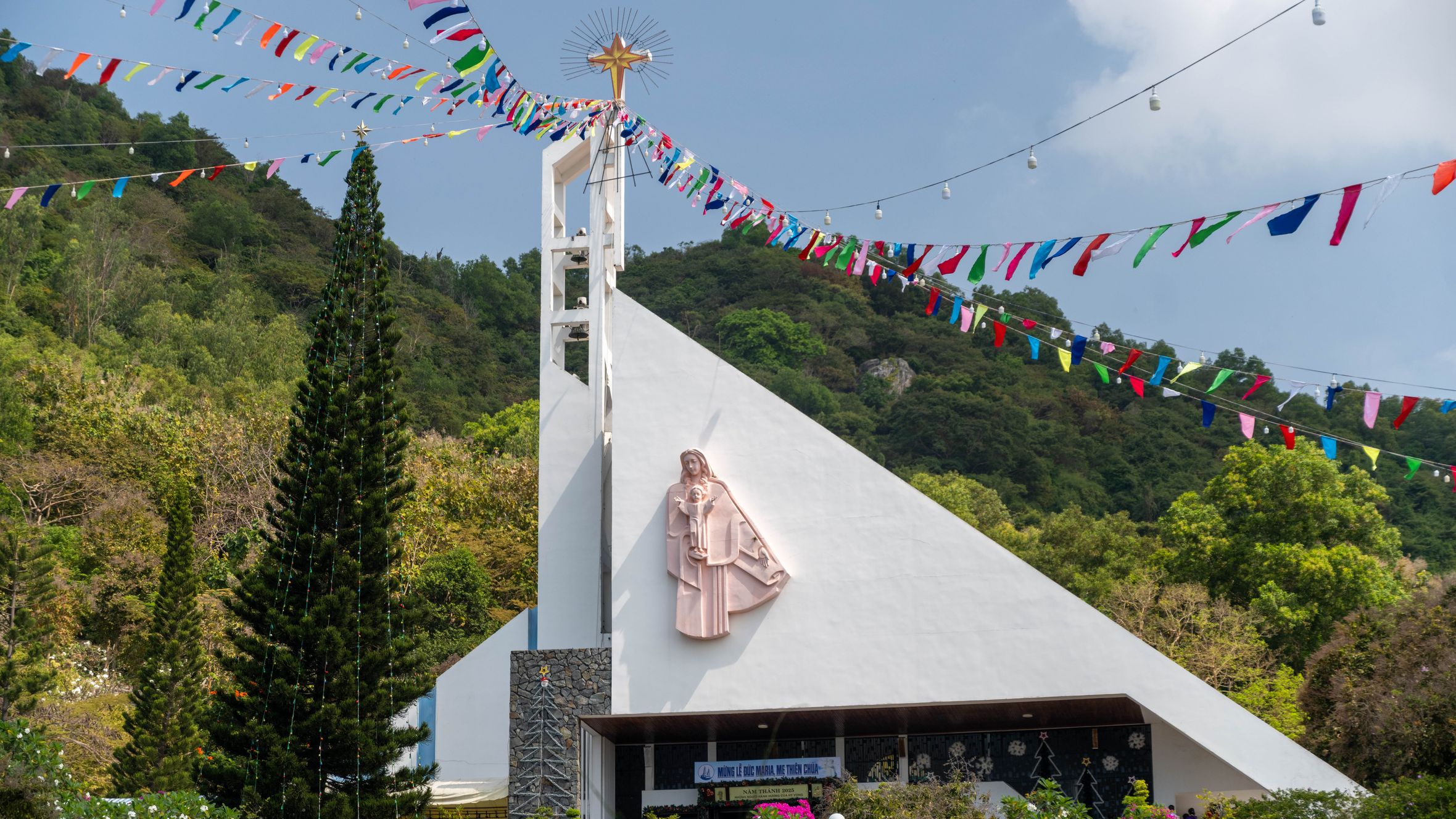 A picturesque church in Vũng Tàu adorned with colorful banners and set against a lush hillside.