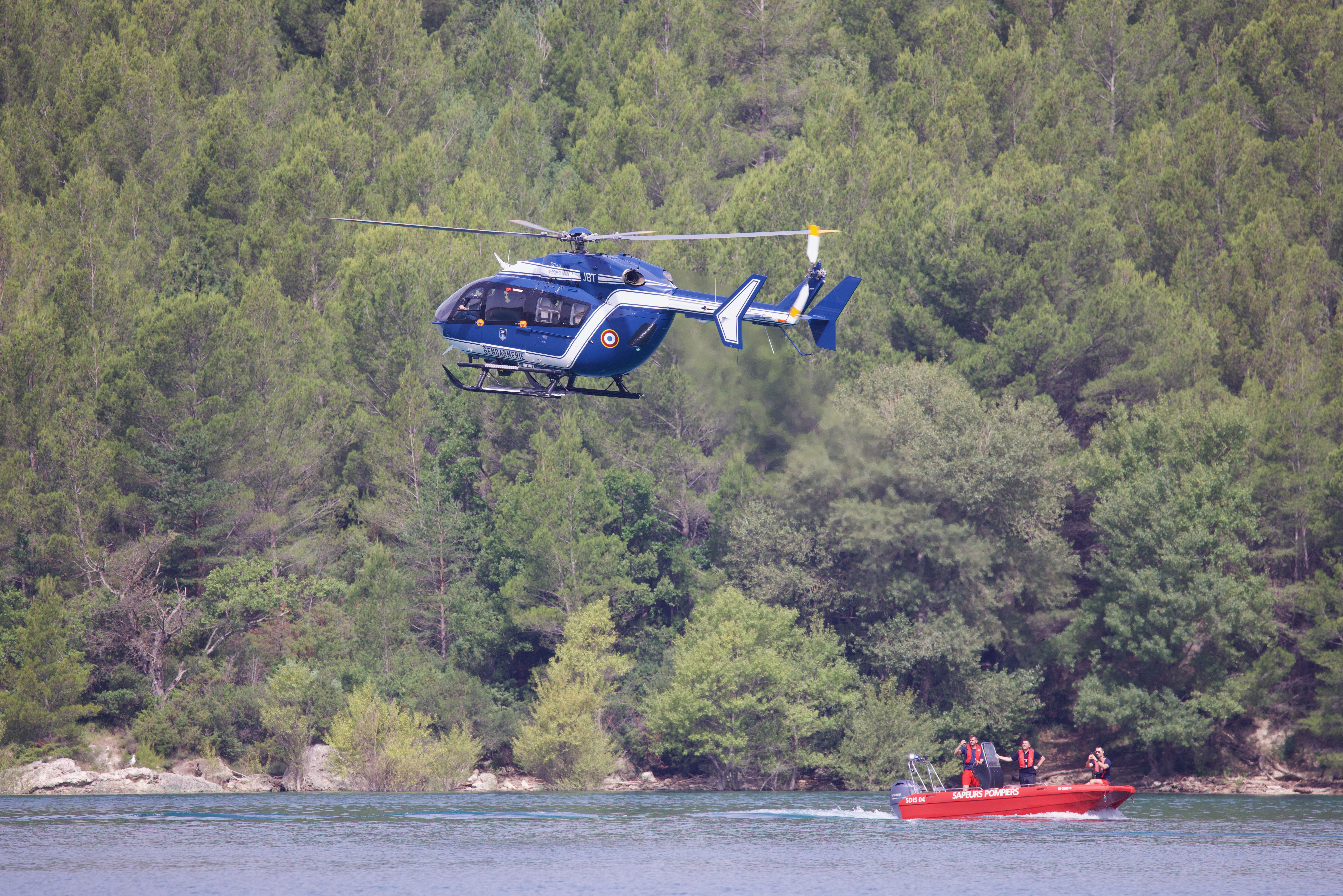 Helicopter Hovering Over Water in Forested Area