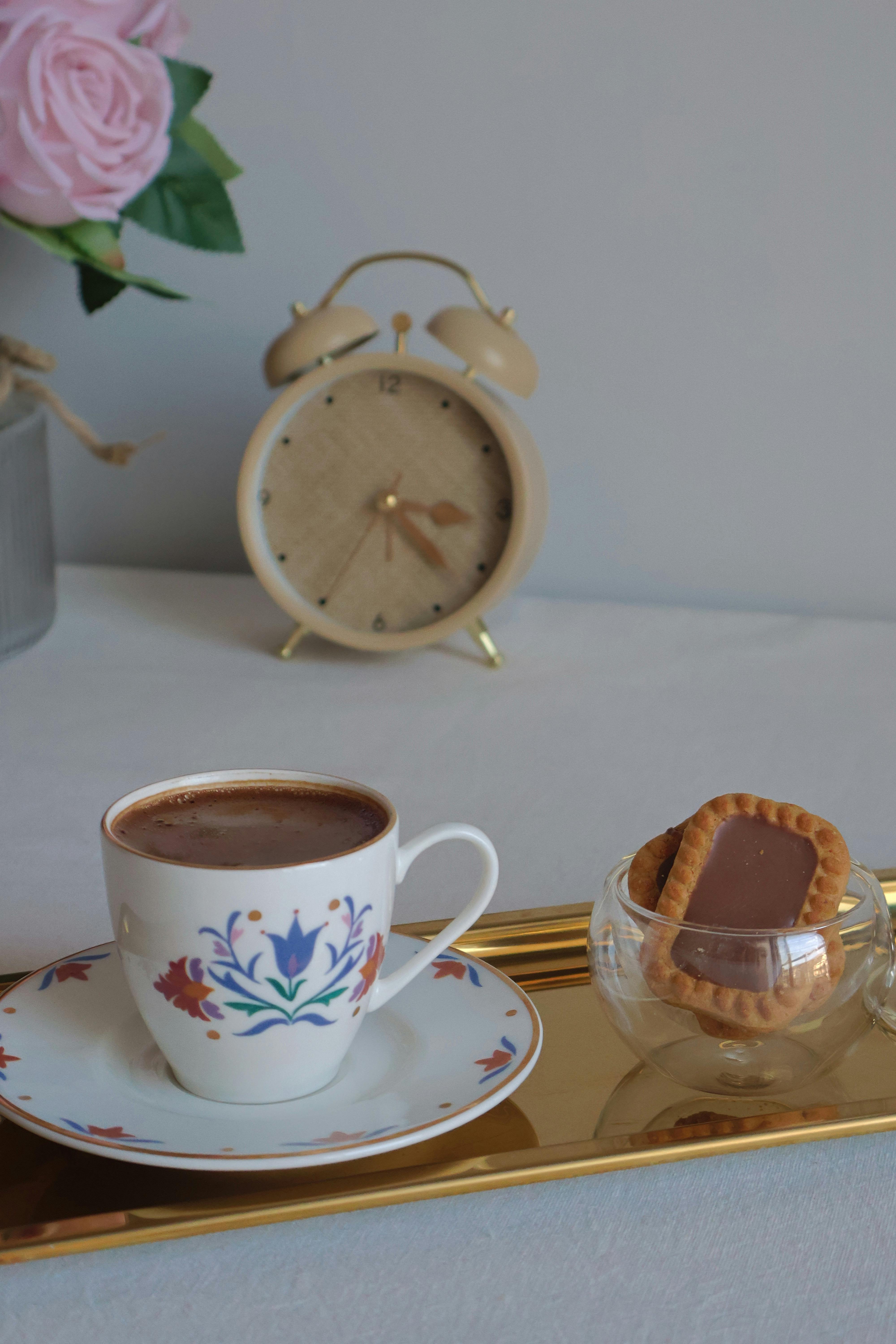 grátis Um elegante conjunto de café com xícara florida, biscoitos, relógio e rosas cor-de-rosa. Foto profissional