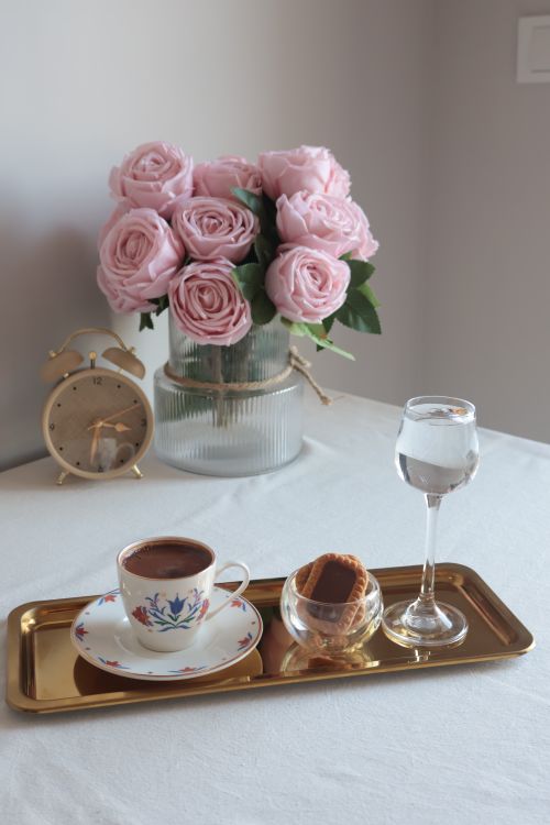 Free A refined arrangement featuring coffee, pink roses, and an alarm clock on a golden tray. Stock Photo