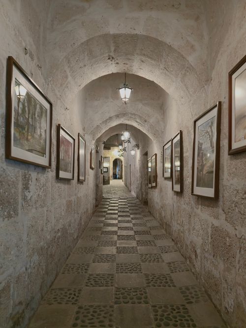 Free A narrow stone hallway adorned with framed artwork and vintage lighting. Stock Photo