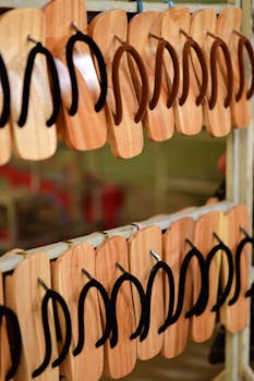 Rows of handmade wooden flip flops with black straps on display in a market setting.