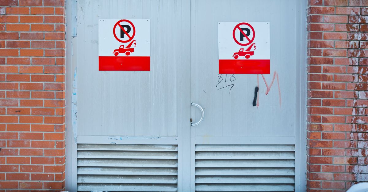 Front view of no parking signs on a metal door framed by a brick wall, with snow on the ground.