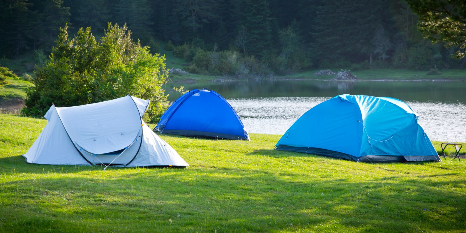 A campsite with tents beside a forested lake in the mountains