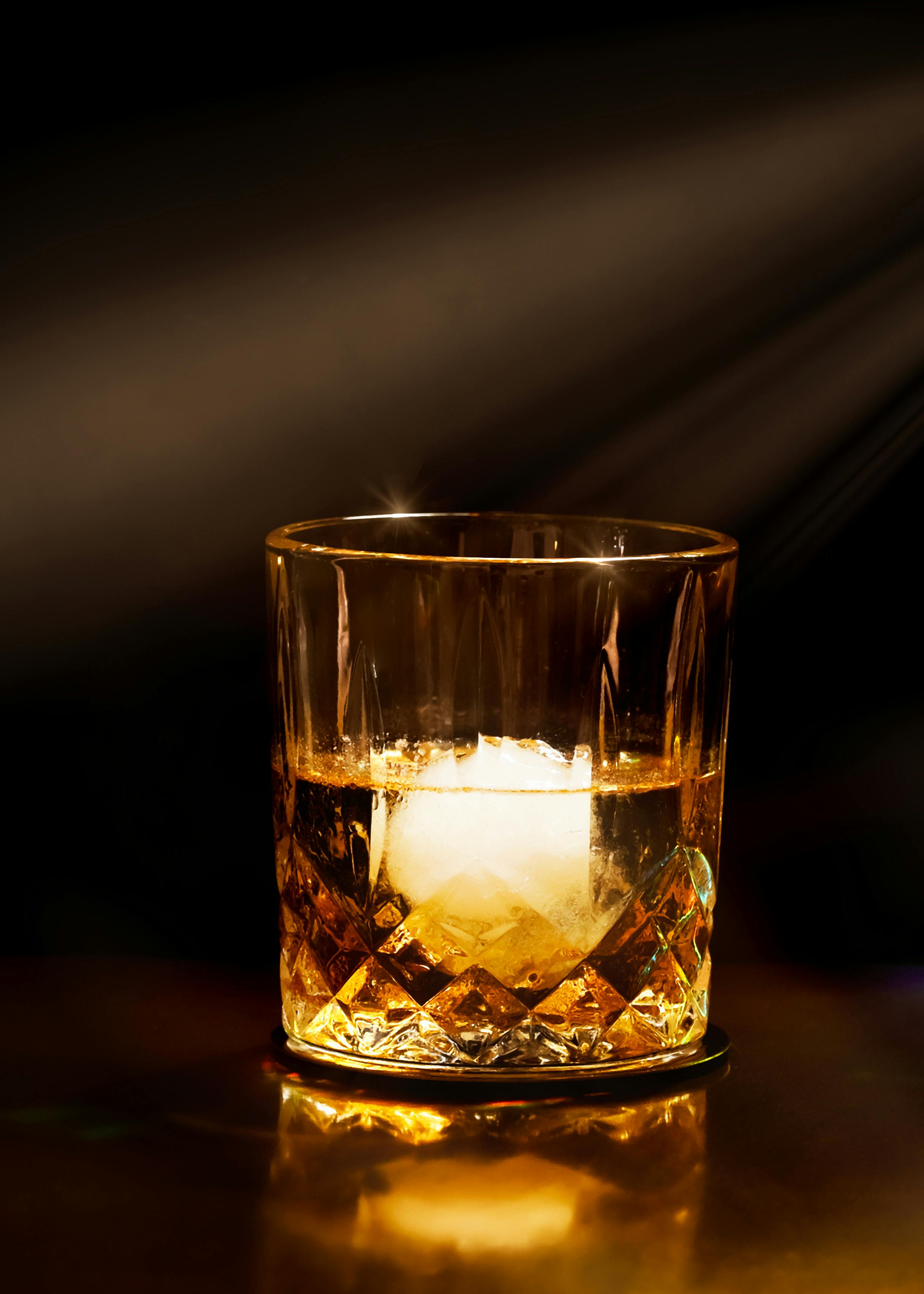 Crystal whiskey glass with ice on a dimly lit bar, exuding elegance and sophistication.