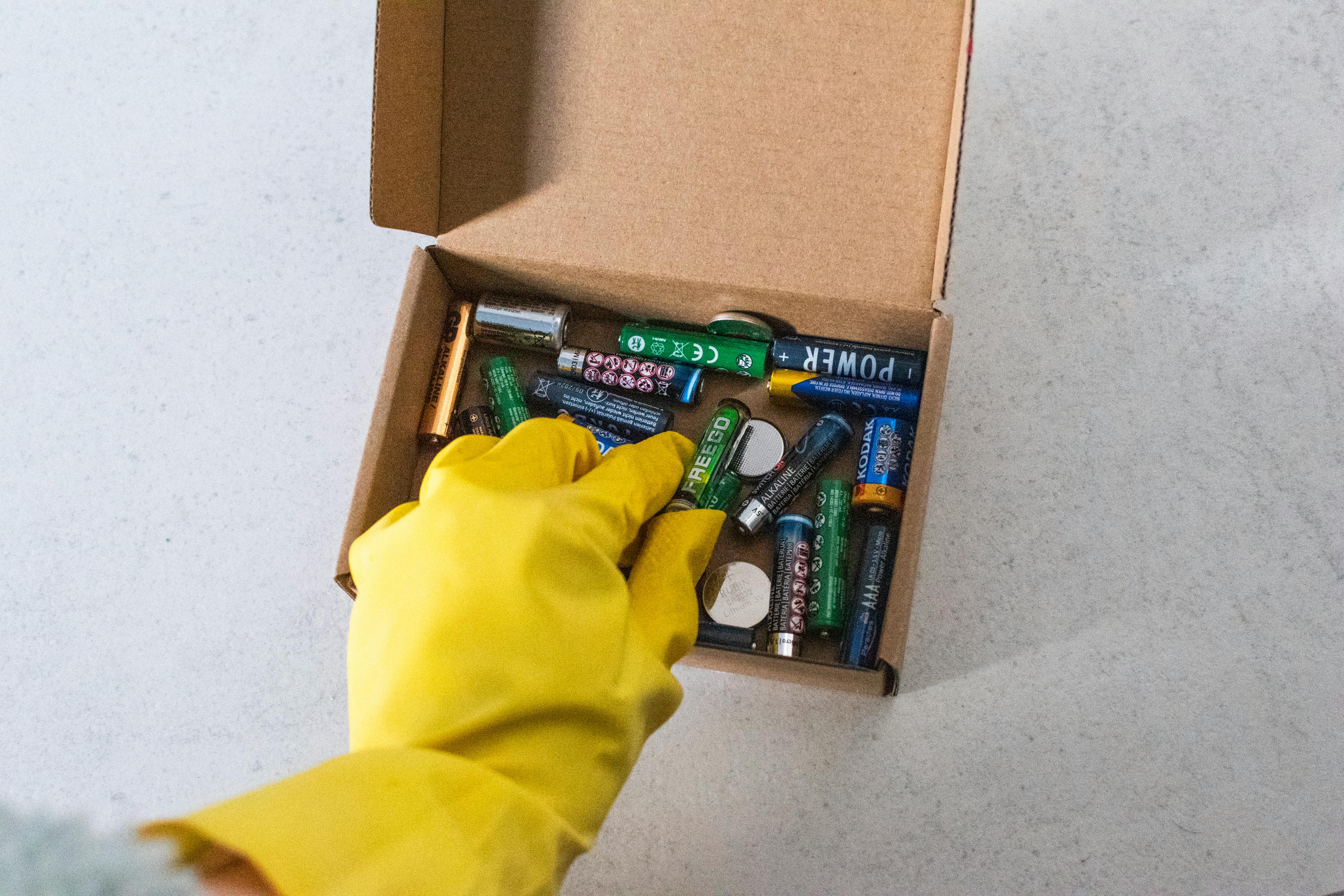 Yellow-gloved hand handling used batteries for safe recycling.