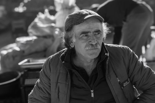 Free Black and white portrait of a middle-aged man in a cap sitting outdoors in a casual setting. Stock Photo