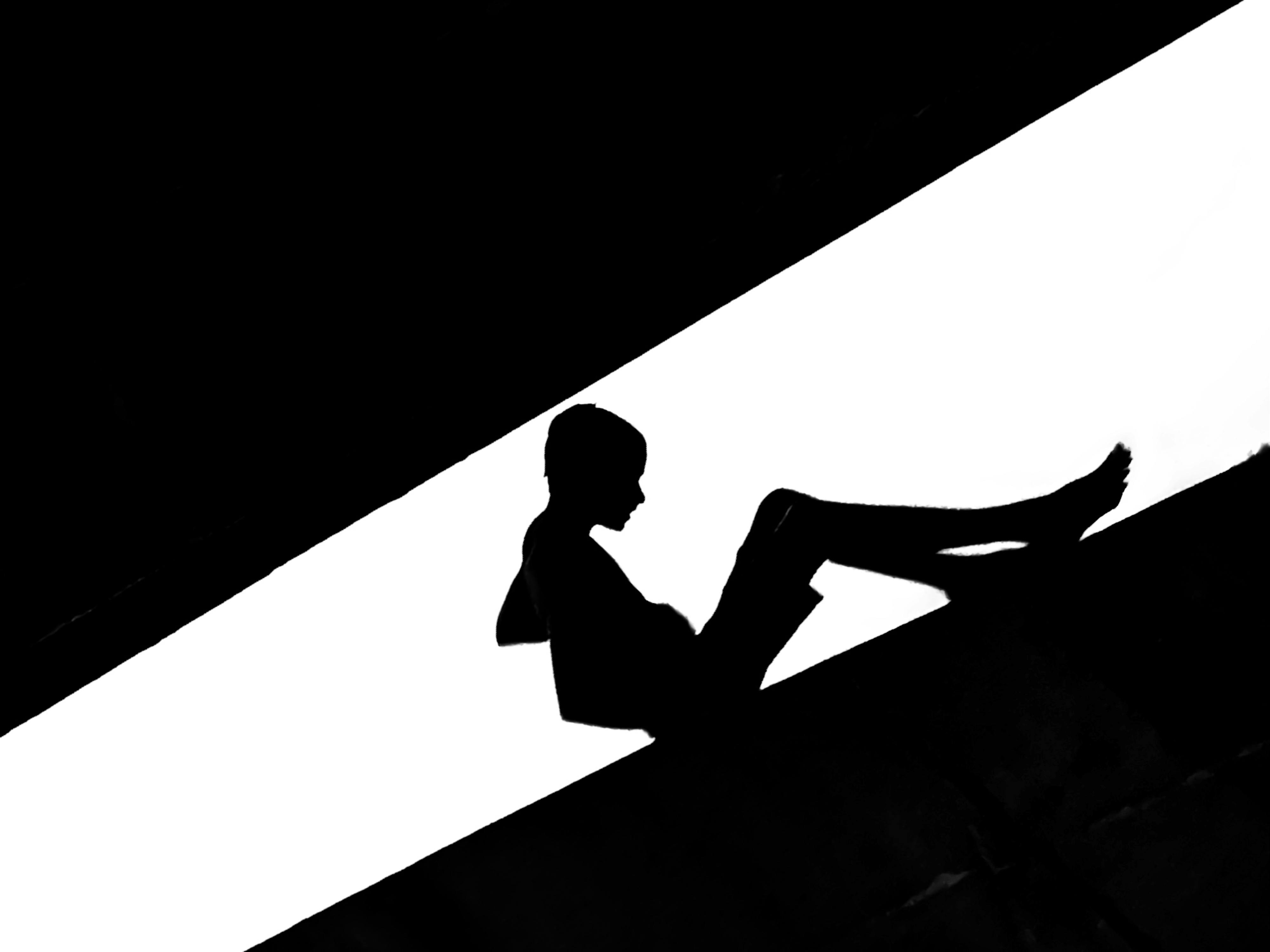 Free Dramatic black and white silhouette of a boy sitting against a bright background in Dhaka. Stock Photo