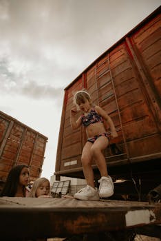 Three children playing by old train cars on a warm day.