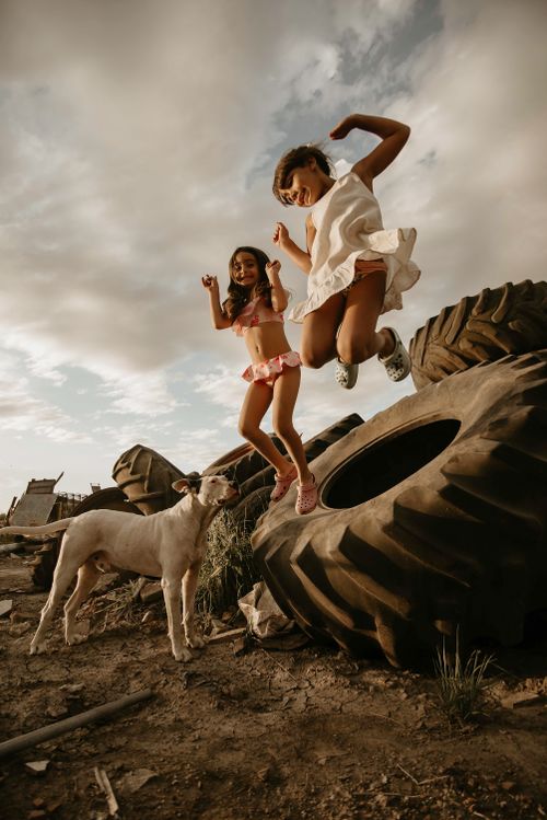 Free Joyful children jumping on old tires with a dog under a cloudy sky. Stock Photo