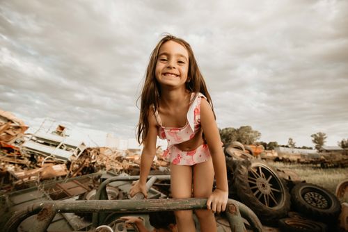 Free Smiling young girl in swimsuit outdoors climbing on metal structure with junkyard background. Stock Photo