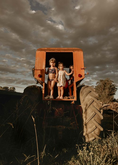 Free Three children enjoy a sunny day playing on an old orange tractor outdoors. Stock Photo
