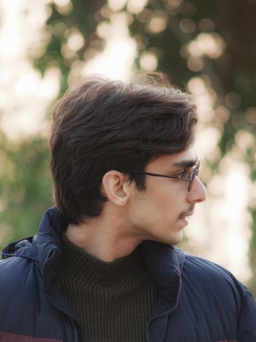Free A thoughtful portrait of a young man wearing glasses and a winter coat, set against a blurred outdoor backdrop. Stock Photo