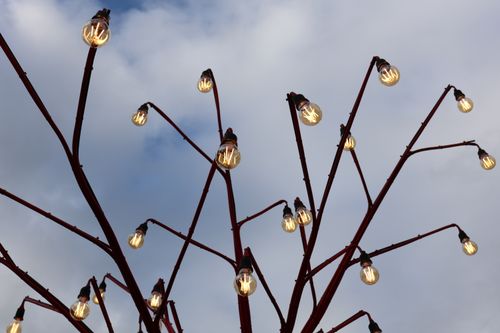 Free Red metal structure with light bulbs against a cloudy sky, creating a unique lighting installation. Stock Photo