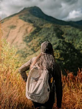 A woman with a backpack hikes towards a mountain under clear skies, embracing nature's beauty.