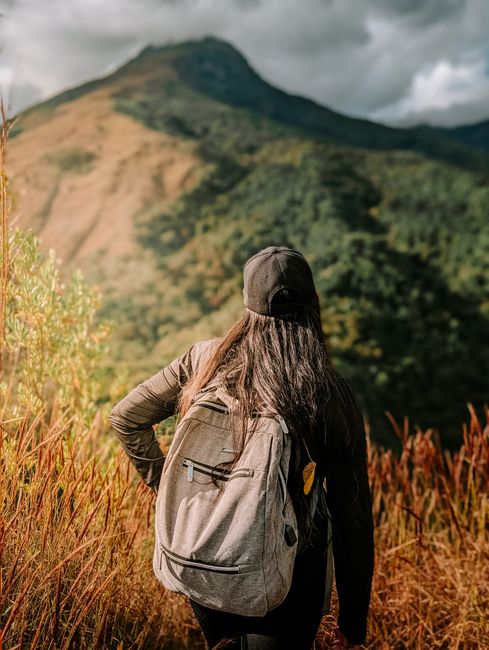 A woman with a backpack hikes towards a mountain under clear skies, embracing nature's beauty.