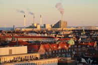 A panoramic view of Copenhagen's skyline featuring a modern factory and traditional architecture.