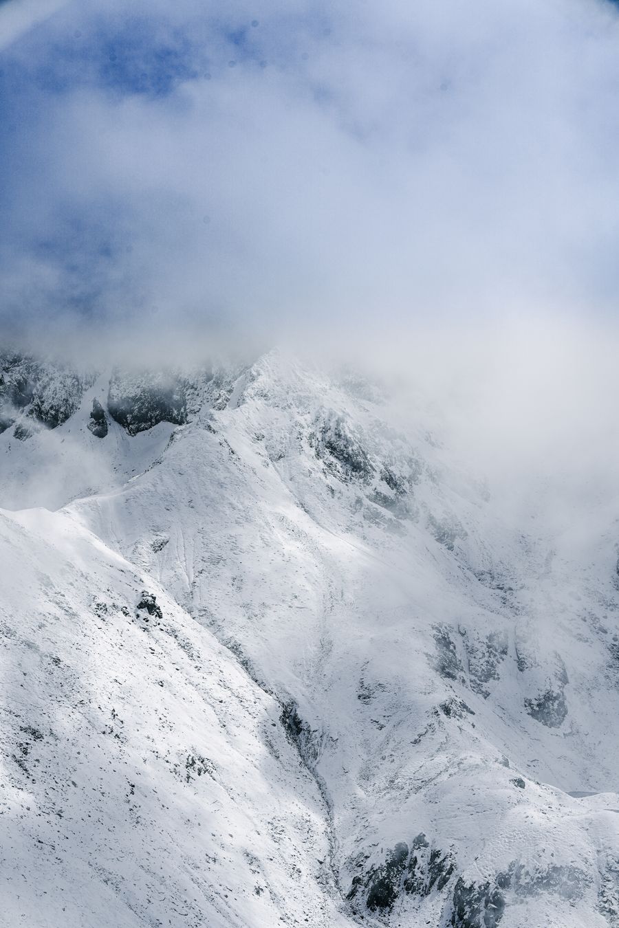 Snow-covered mountain ridge half buried in cloud — photo by SERHAT TUĞ on Pexels