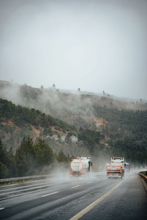 Free Trucks navigate a foggy, rainy mountain road with mist and greenery. Stock Photo