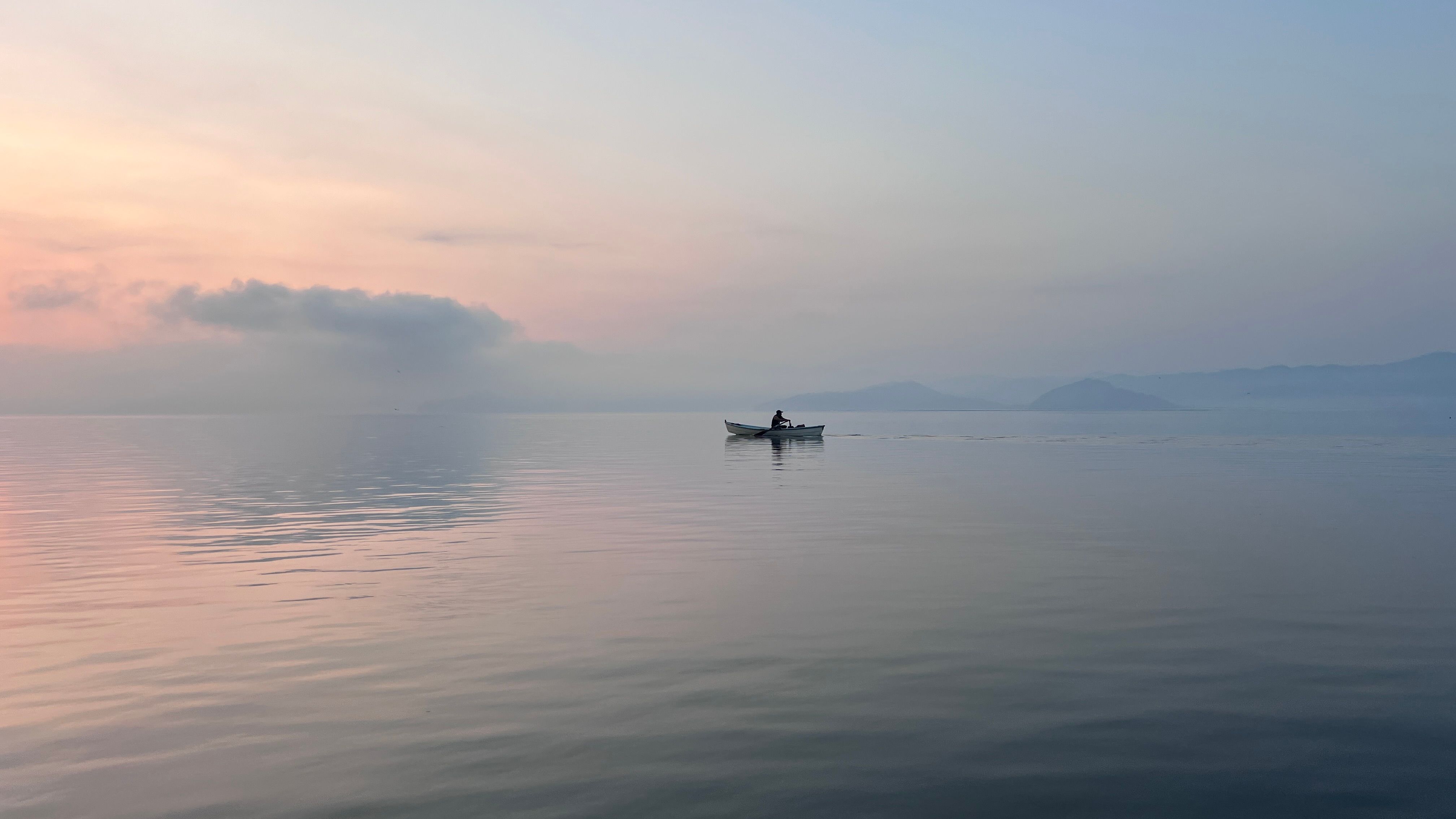A lone boat on a tranquil lake during sunrise with soft pastel hues in Mexico.