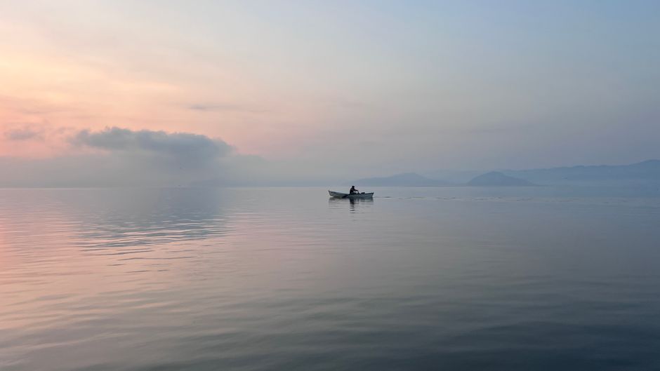 A lone boat on a tranquil lake during sunrise with soft pastel hues in Mexico.