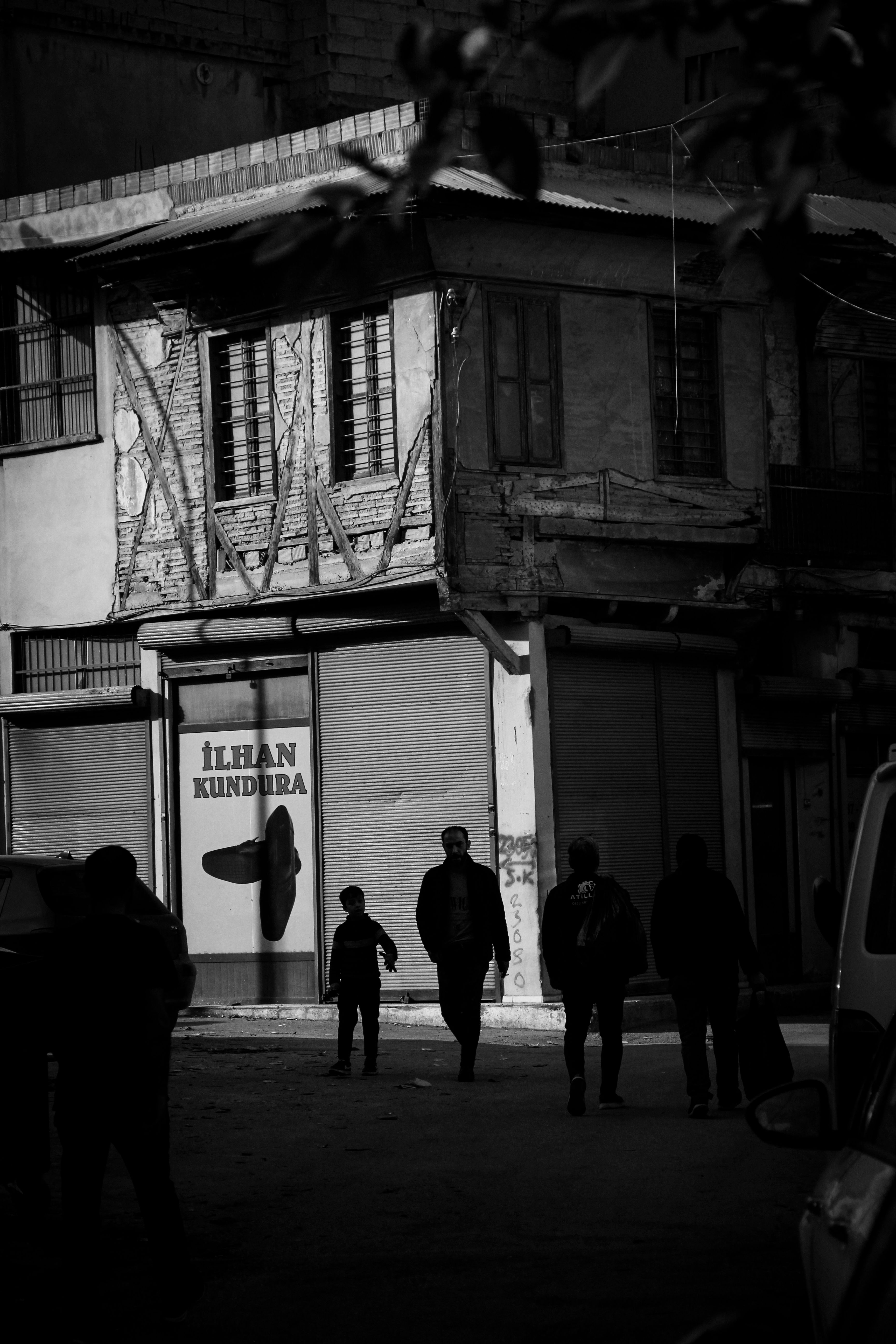 Black and white photo of silhouettes passing an old building with a Turkish sign.