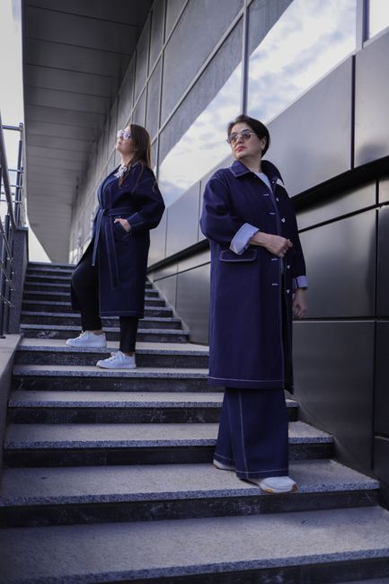 Two women in stylish coats pose on a modern urban staircase, exuding confidence and style.