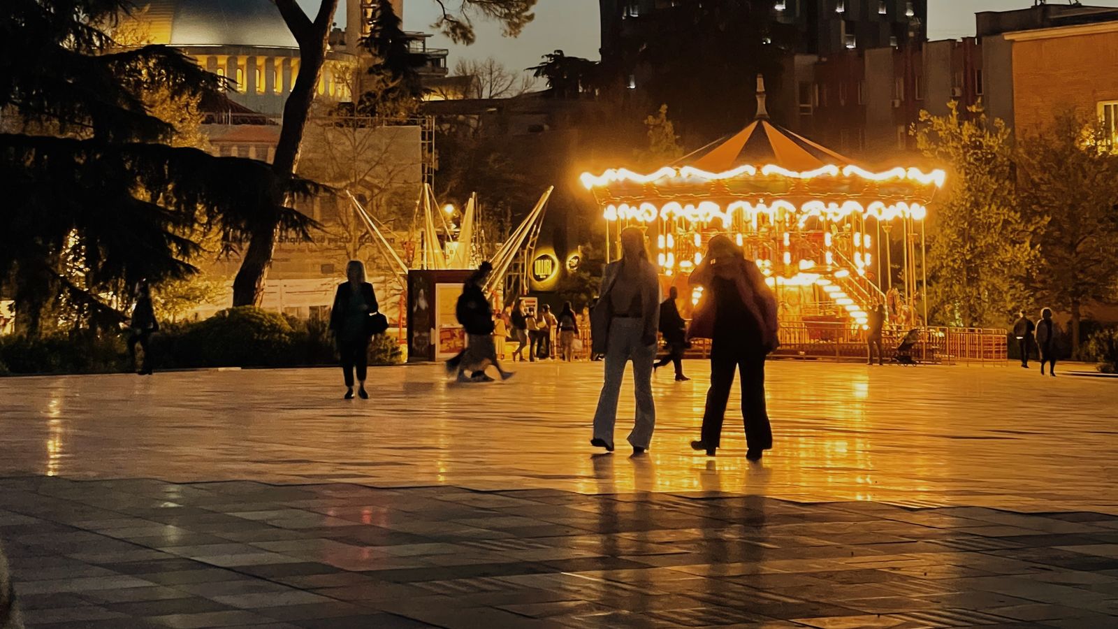 Skanderbeg Square in Tirana at dusk, with a lit carousel, a mosque dome and a modern tower