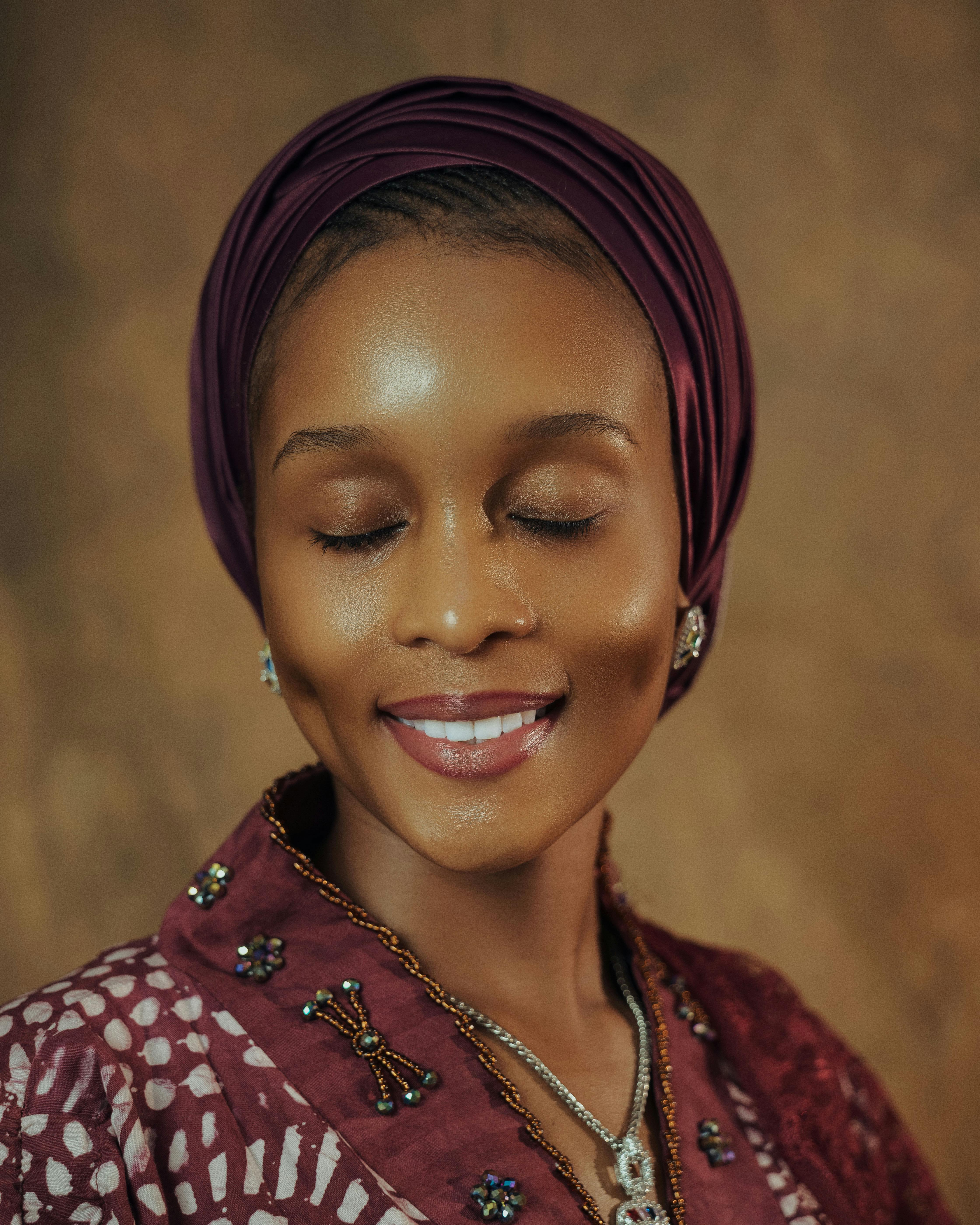 grátis Retrato em close-up de uma mulher sorridente usando um elegante turbante e joias, com os olhos fechados. Foto profissional
