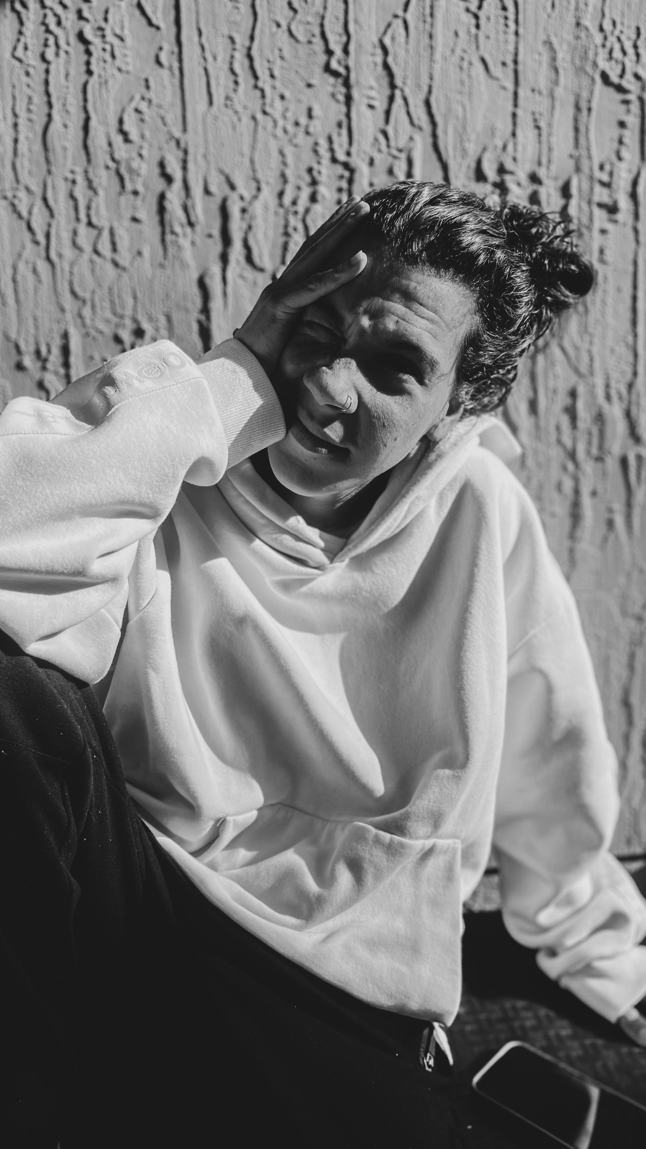Black and white portrait of a woman in casual wear outdoors, enjoying the sunlight against a textured wall.