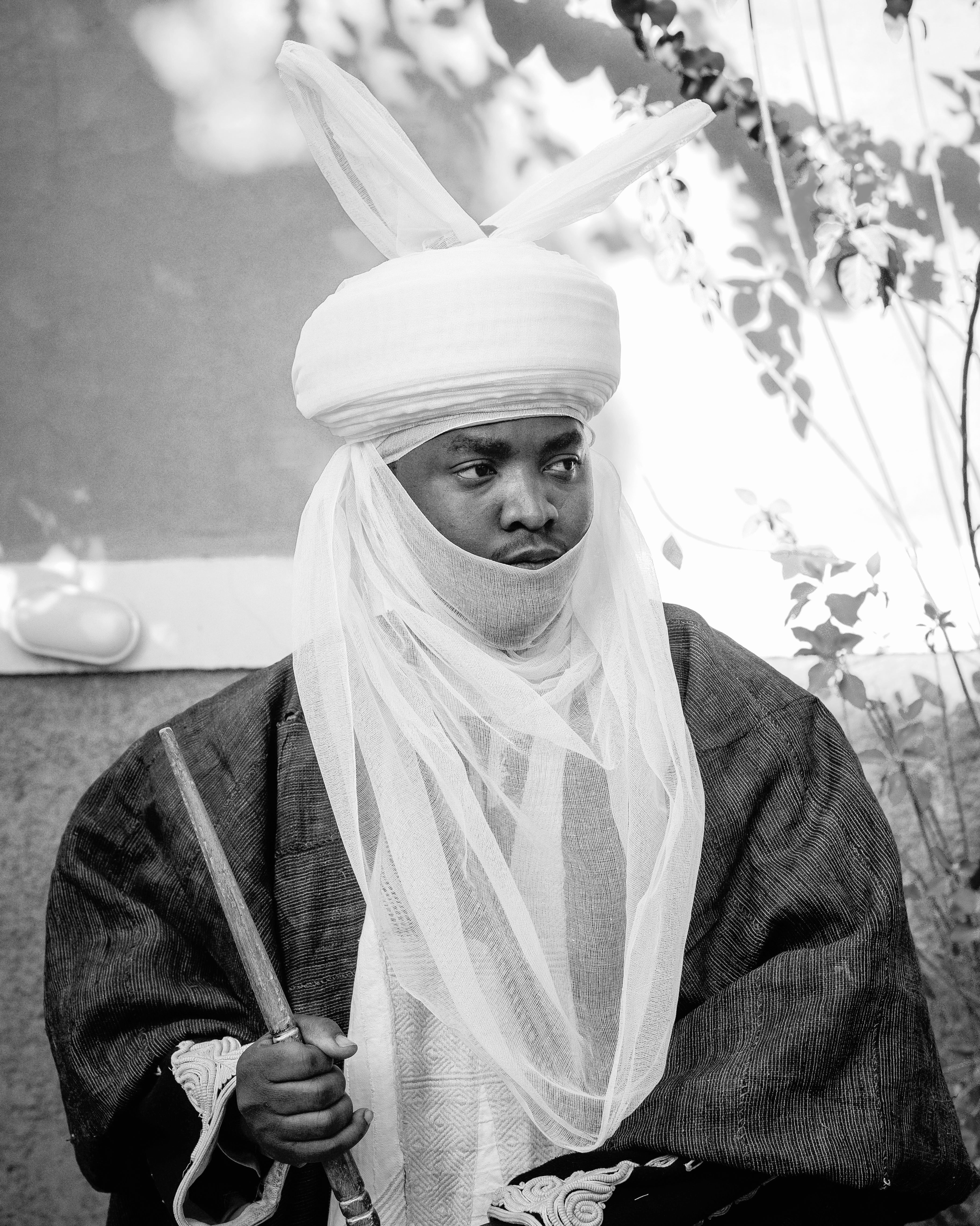 Man in traditional African regalia holding a sword, featuring a turban and veil.