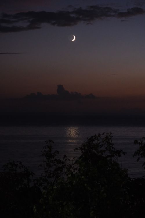 Free Peaceful twilight scene with crescent moon reflecting on calm ocean waters. Stock Photo