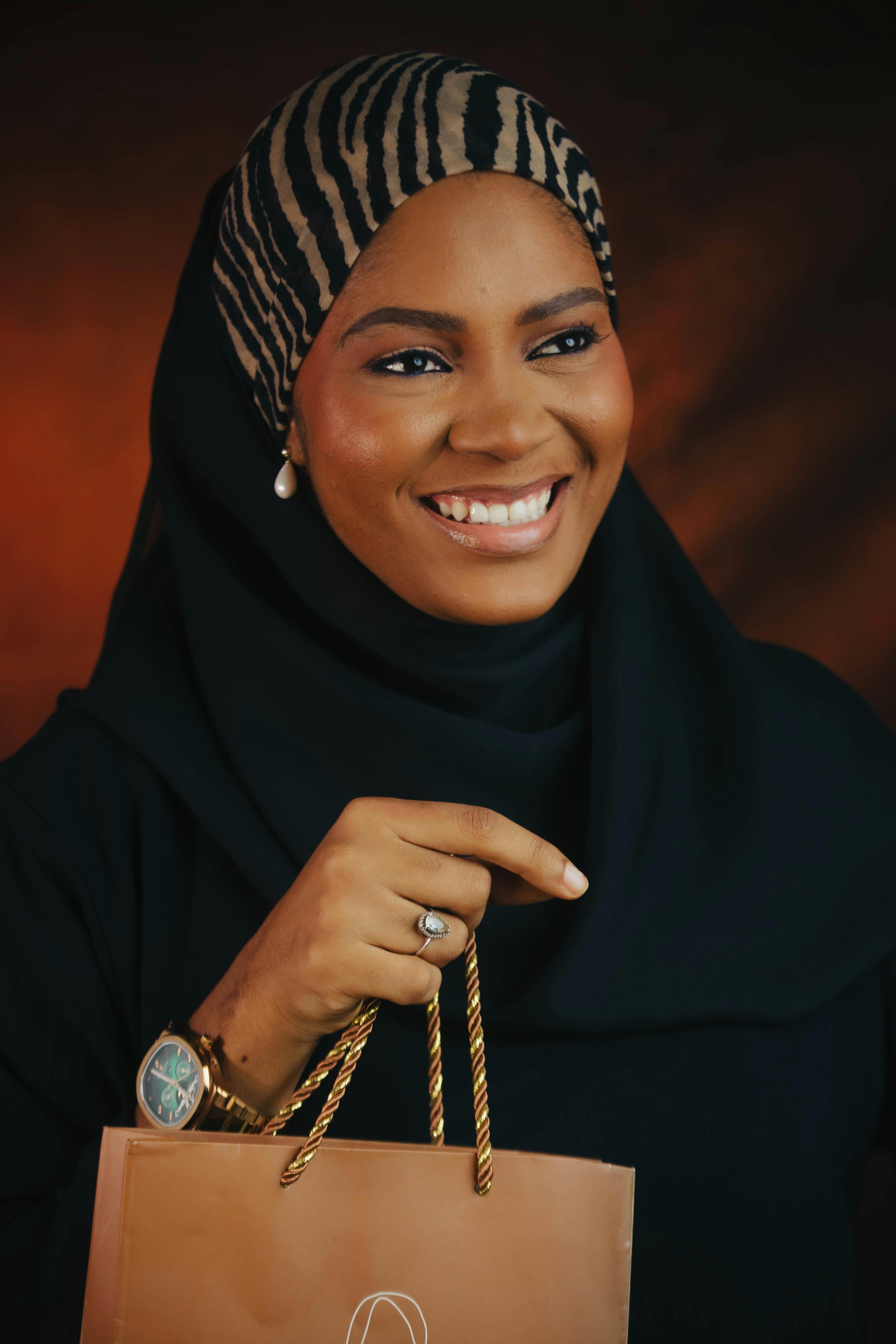 Zadarmo Usmievavá žena v hidžábe držiaca nákupnú tašku, vyjadrujúca eleganciu a modernú módu. Fotka z fotobanky