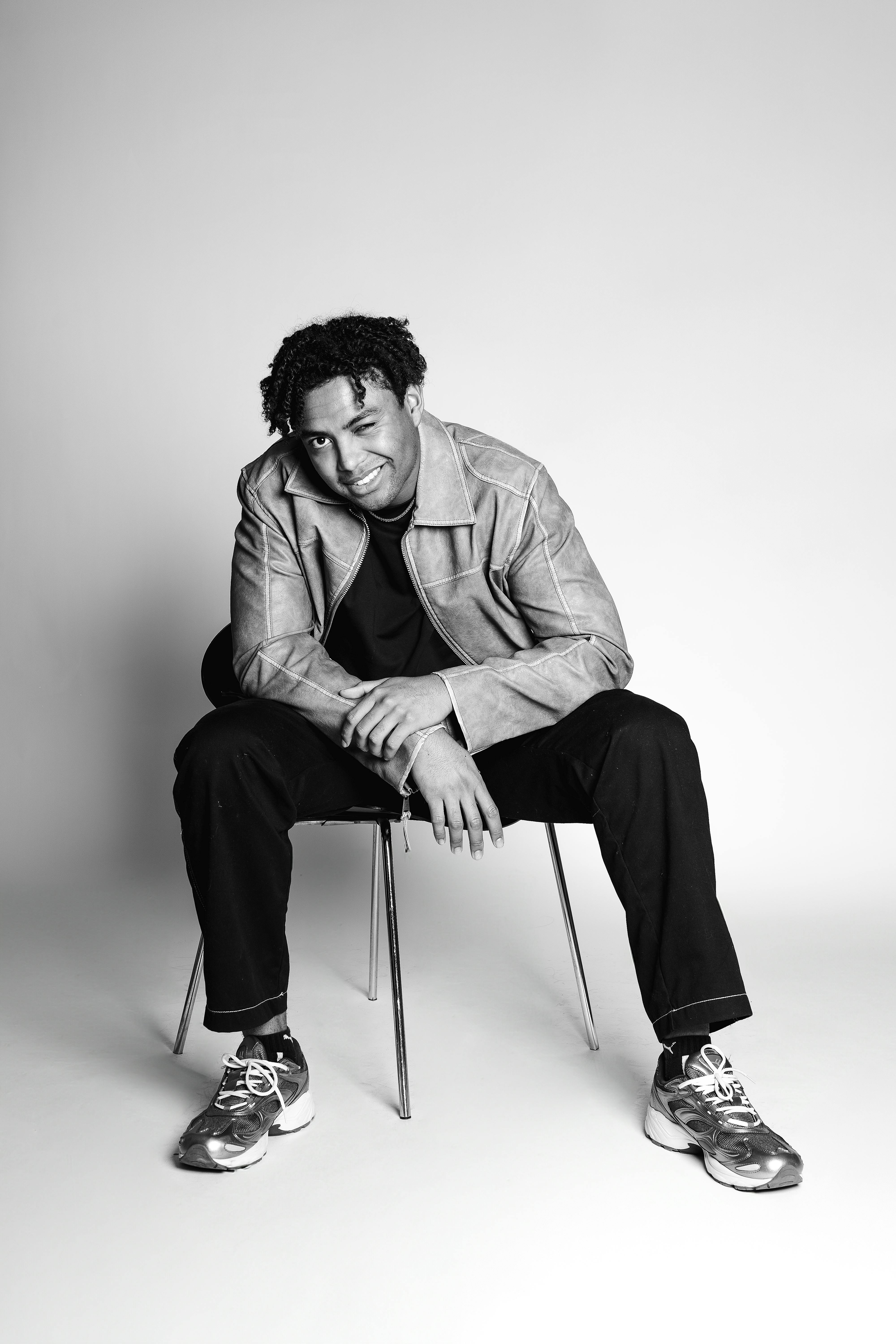 grátis Retrato monocromático de um jovem adulto elegante sentado em uma cadeira. Foto profissional